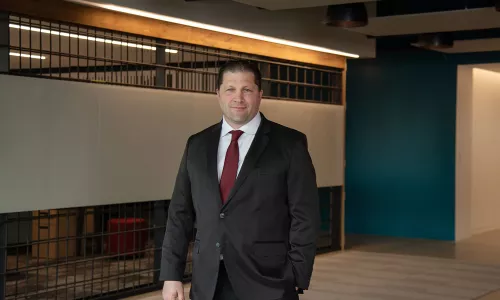 A man in professional wear stands in a hallway.