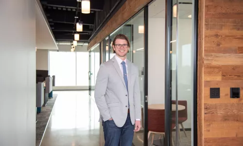 A man in professional wear stands in a hallway.