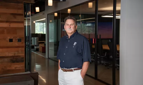 A man in professional wear stands in a hallway.