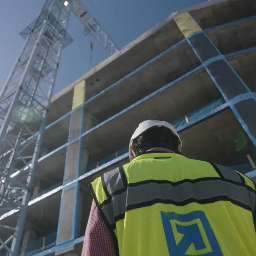 A man in construction gear looks up at a tower crane.