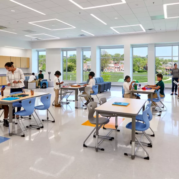 School classroom with a teacher and groups of students at desks.