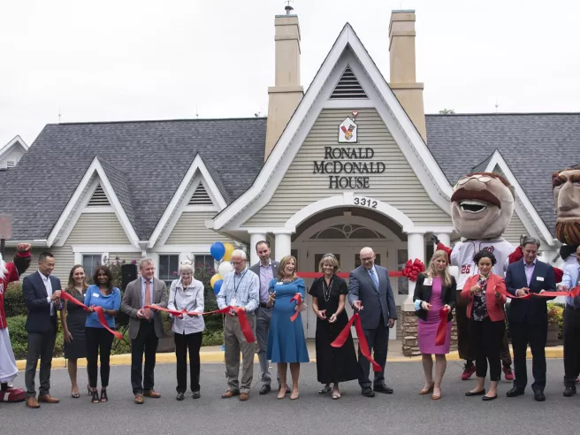 Group of people cutting red ribbon in front of Ronald McDonald House