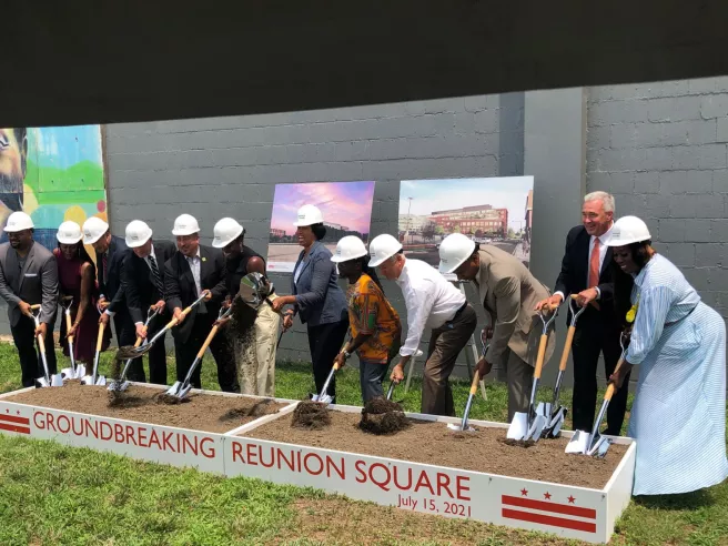 Line of people wearing hard hats with shovels poised to dig into dirt